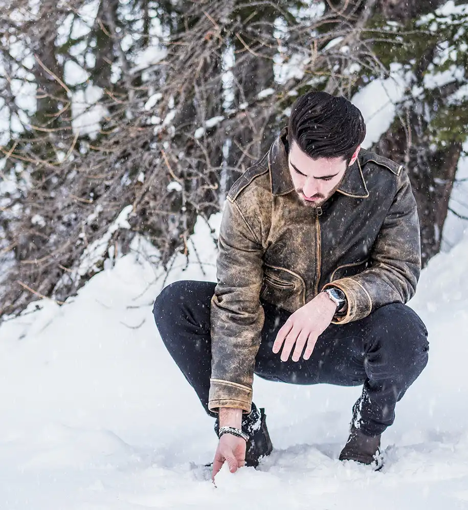 Junger Mann in Vintage Lederjacke hockt vor verschneitem Wald - Cleanteam Leder- und Pelzreinigung