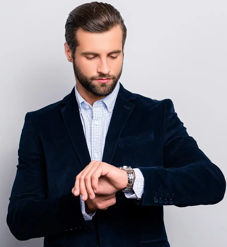 Junger Mann in perfekt gepflegtem marineblauen Samtanzug schaut auf seine Armbanduhr