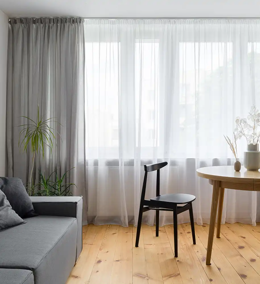 Gemütliches Wohnzimmer mit grauer Couch und Esstisch vor Fenster mit grauem Vorhang und Gardinen