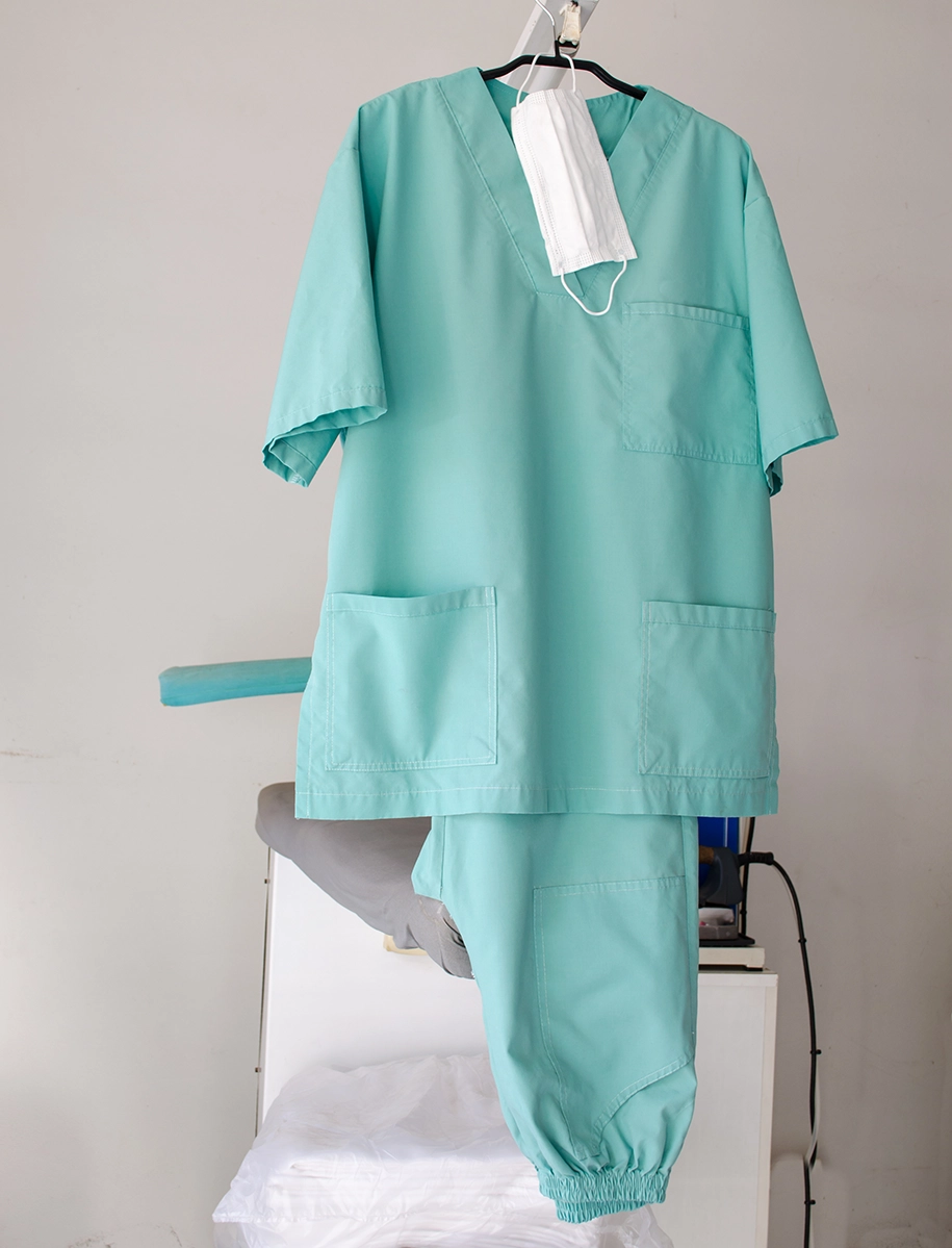 Grüne medizinische Uniform und Maske hängen an einem Kleiderbügel in einer Wäscherei.